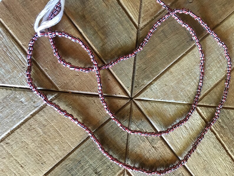 May include: A strand of red, white, and black beads. The beads are small and round, and they are strung together on a thin cord.