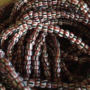 May include: A close-up of a pile of red, white, and black striped glass beads. The beads are small and round, and they are arranged in a random pattern.