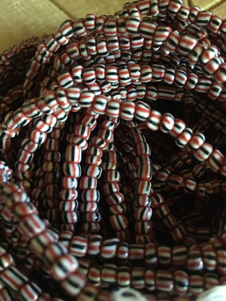 May include: A close-up of a pile of red, white, and black striped glass beads. The beads are small and round, and they are arranged in a random pattern.
