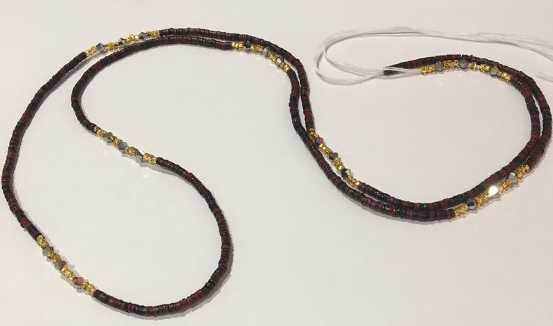 May include: A double-strand beaded necklace with black and red beads, gold beads, and silver beads. The necklace is tied with a white string.