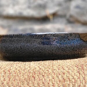 May include: A small, black ceramic bowl with a textured, crackled glaze. The bowl is slightly oval-shaped and has a rounded rim.