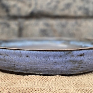 May include: A blue and brown ceramic bowl with a slightly rounded rim. The bowl has a speckled glaze and a rustic appearance.