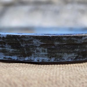 May include: A round, blue and black ceramic dish with a slightly raised rim. The dish has a rustic, hand-crafted look.