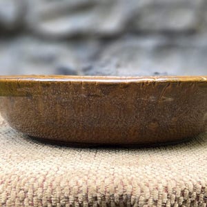 Puede incluir: Un cuenco de cerámica marrón con una superficie ligeramente texturizada. El cuenco está sobre una superficie de arpillera.