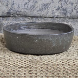 May include: A dark gray ceramic bowl with a rounded rectangular shape. The bowl has a smooth, slightly textured surface.