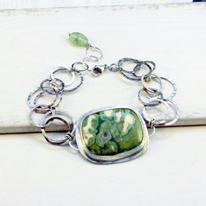 May include: A silver bracelet with a green and white stone pendant. The bracelet is made of interconnected silver circles.