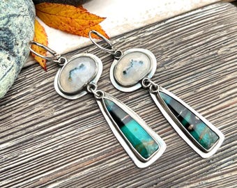 May include: A pair of silver-toned dangle earrings. Each earring features an oval-shaped, white stone with blue and gray inclusions, connected to a long, trapezoid-shaped stone with turquoise and black accents. The earrings have a lever-back closure.