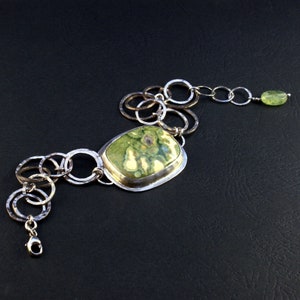 May include: A silver chain bracelet with a green and white stone pendant. The chain is made of interconnected circles and the pendant is set in a silver frame.