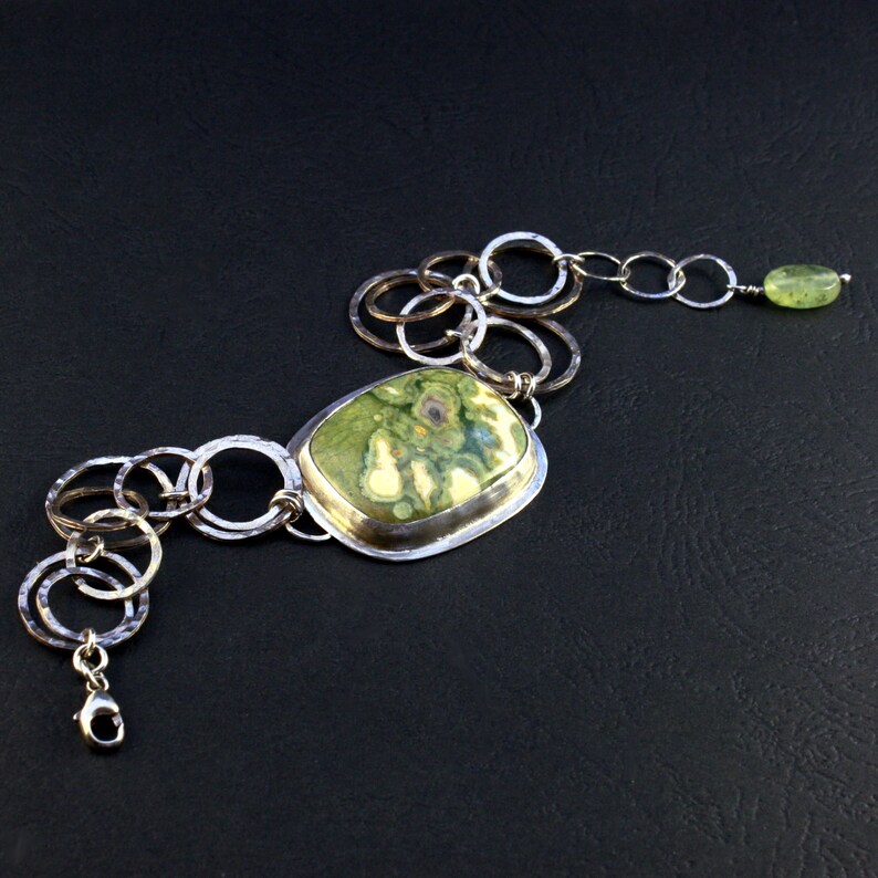 May include: A silver chain bracelet with a green and white stone pendant. The chain is made of interconnected circles and the pendant is set in a silver frame.