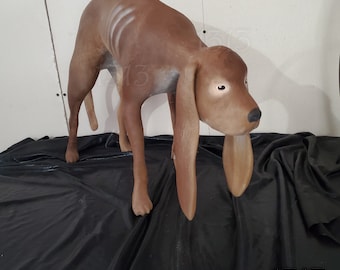 Puede incluir: Una escultura de perro de cerámica marrón con orejas largas y caídas. El perro está de pie sobre una superficie de tela negra.