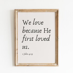 Puede incluir: Una impresión enmarcada con el texto "Amamos porque Él nos amó primero." y la referencia bíblica "1 Juan 4:19".