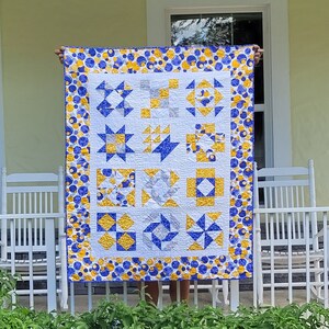 May include: A quilt with a white background and a variety of blue and yellow geometric patterns. The quilt is surrounded by a border of blue and yellow polka dots.