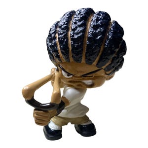 May include: A brown and black cartoon figure with a slingshot. The figure has black hair in braids and is wearing a white shirt and brown pants.