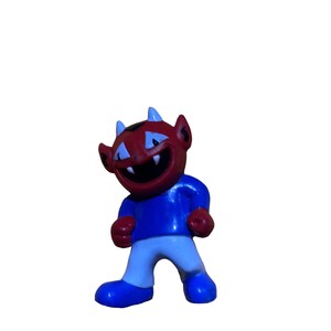 May include: A red and blue devil figurine with a wide grin and horns. The figurine is standing with its legs spread apart and its arms at its sides.