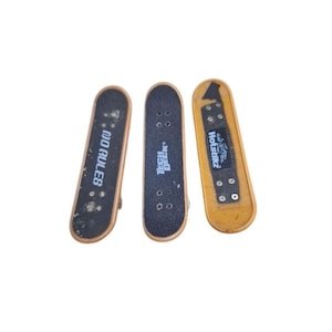 Pode incluir: Três mini-skates. Um tem o texto "NO RULES" em branco, outro "Tech Deck" em branco e o terceiro "Hotstufz" em branco. Os skates são pretos, castanhos e amarelos.