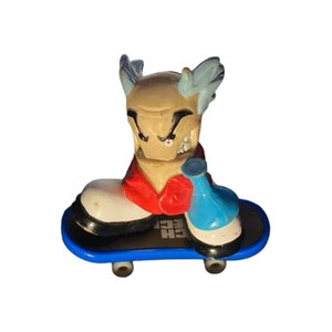 May include: A blue and white skateboard with a cartoon figure on top. The figure has a red shirt, blue pants, and white hair. The figure is holding a blue object in its right hand.