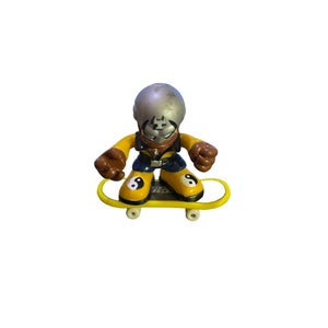 May include: A yellow and black skateboard with a figure on top. The figure is wearing a silver helmet, a black and blue shirt, and yellow and black shoes with yin yang symbols.