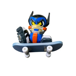 May include: A blue and orange toy figure with a black helmet and yellow eyes riding a blue skateboard with white wheels.