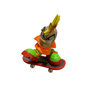 May include: A Tech Deck skateboard figure with a cartoonish design. The figure has a tan head with a yellow mohawk and orange collar. The figure is wearing green and red shoes and is riding a red and black skateboard.