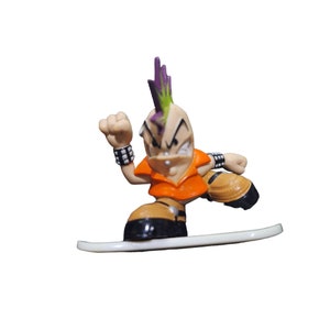 May include: A small plastic figurine of a punk rock character with a mohawk, wearing an orange shirt and black wristbands, riding a white snowboard.