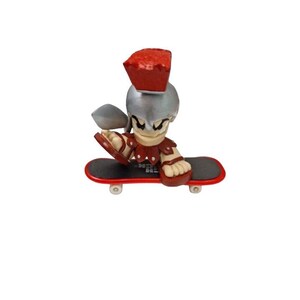 May include: A red and silver toy figure of a Roman soldier riding a fingerboard skateboard. The figure is wearing a helmet and a red tunic. The skateboard is red and black.
