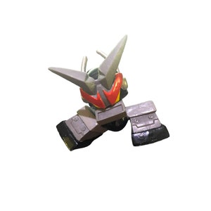 May include: A gray and black robot toy with red eyes. The robot has a pointed head and two arms with hands. The robot is in a crouching position.