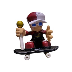 Puede incluir: Una figura de patinador artístico rojo y blanco con gafas de sol azules, sosteniendo un micrófono dorado y blanco, de pie sobre una patineta negra con ruedas blancas.