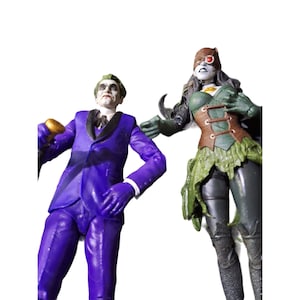 Puede incluir: Una figura de acción del Joker con un traje morado y una figura de acción de Poison Ivy verde y marrón. El Joker sostiene un bastón y tiene una sonrisa traviesa. Poison Ivy lleva un traje verde y marrón con una falda de hojas y una máscara roja para los ojos.