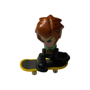 May include: A red-haired fingerboard character with a skull and crossbones belt buckle rides a yellow skateboard with black wheels.