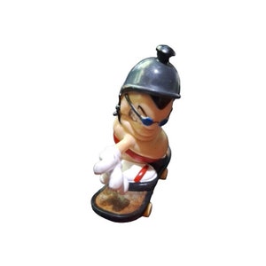 May include: A black and white figurine of a person wearing a black helmet and sunglasses, riding a skateboard. The figurine is made of plastic and has a cartoonish style.