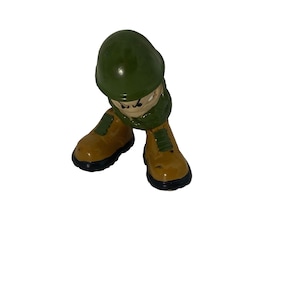 Puede incluir: Una figurita de juguete de plástico verde y marrón de un soldado con un casco verde y botas marrones.