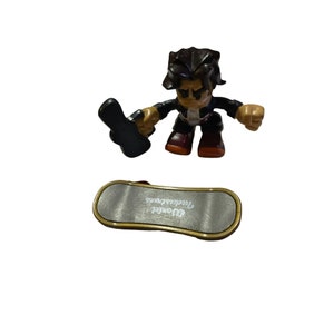 May include: A black and brown figurine of a skateboarder holding a skateboard. The skateboarder is wearing a black jacket, black pants, and red shoes. The skateboard is silver and has the words "World Industries" printed on it.
