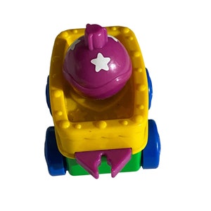 May include: A yellow toy wagon with a purple and white star-shaped ball inside. The wagon has blue wheels and a green base.