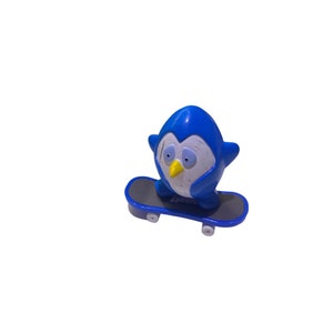 May include: A blue penguin figurine riding a blue and black skateboard with black wheels.