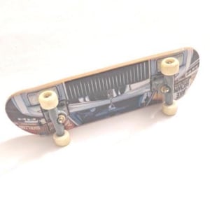 May include: A miniature skateboard with a wooden deck featuring a graphic of a vintage car. The skateboard has silver trucks and cream-colored wheels. The deck has a light brown wood grain.