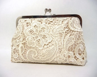 May include: A rectangular clutch bag featuring a cream-colored satin base overlaid with intricate white floral lace. The bag is secured with a silver-toned metal frame and a kiss-lock clasp closure at the top, providing a structured and elegant appearance.