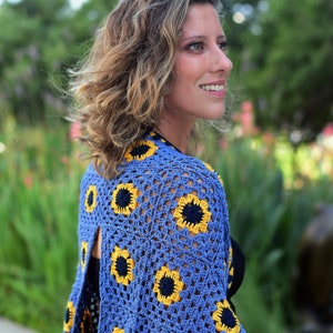 May include: A blue crochet top with a sunflower design. The top has a loose fit and a wide neckline. The sunflower design is made with yellow and black yarn.