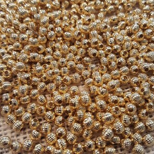 May include: A large pile of gold-colored metal beads. The beads are round and have a textured surface.