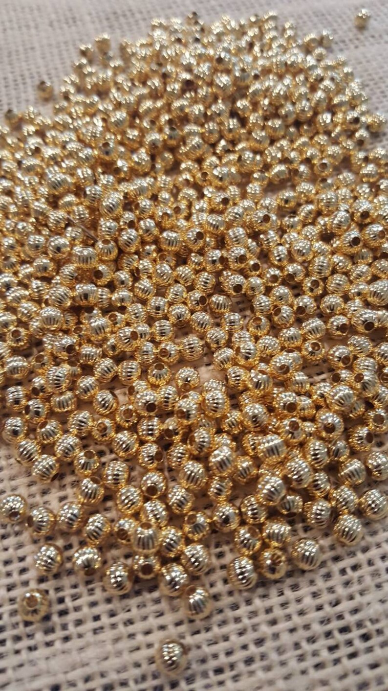 May include: A large pile of gold-colored metal beads. The beads are round and have a textured surface.