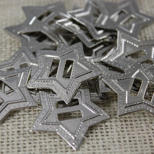 May include: A pile of silver metal star-shaped embellishments with a cutout in the center. The stars have a textured edge.