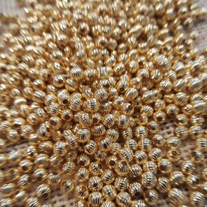 May include: A large pile of gold-colored metal beads. The beads are round and have a textured surface.