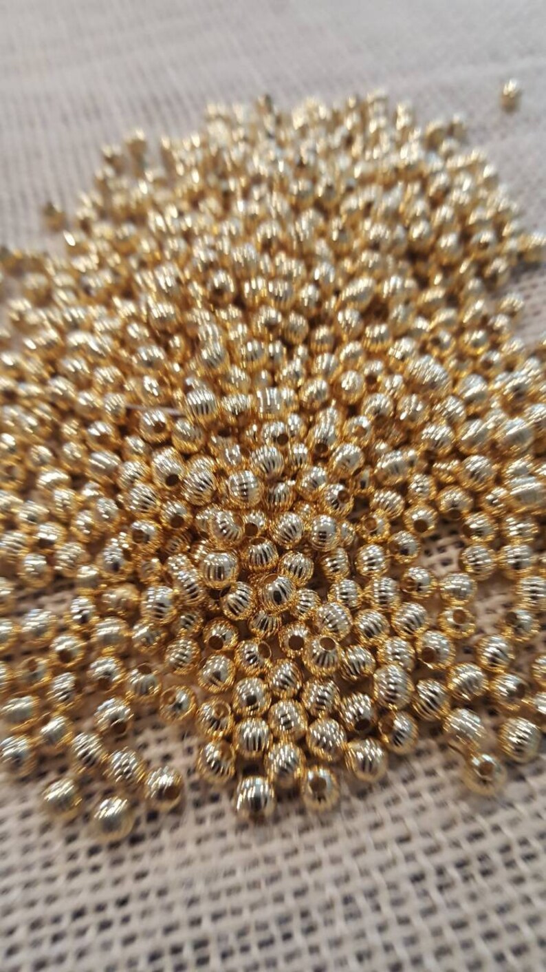 May include: A large pile of gold-colored metal beads. The beads are round and have a textured surface.