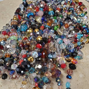 May include: A large assortment of colorful crystal beads in various shapes and sizes. The beads are strung on clear thread and are ready for jewelry making.