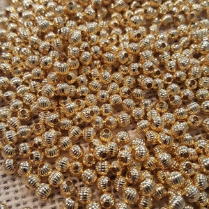May include: A large pile of gold-colored metal beads. The beads are round and have a textured surface.