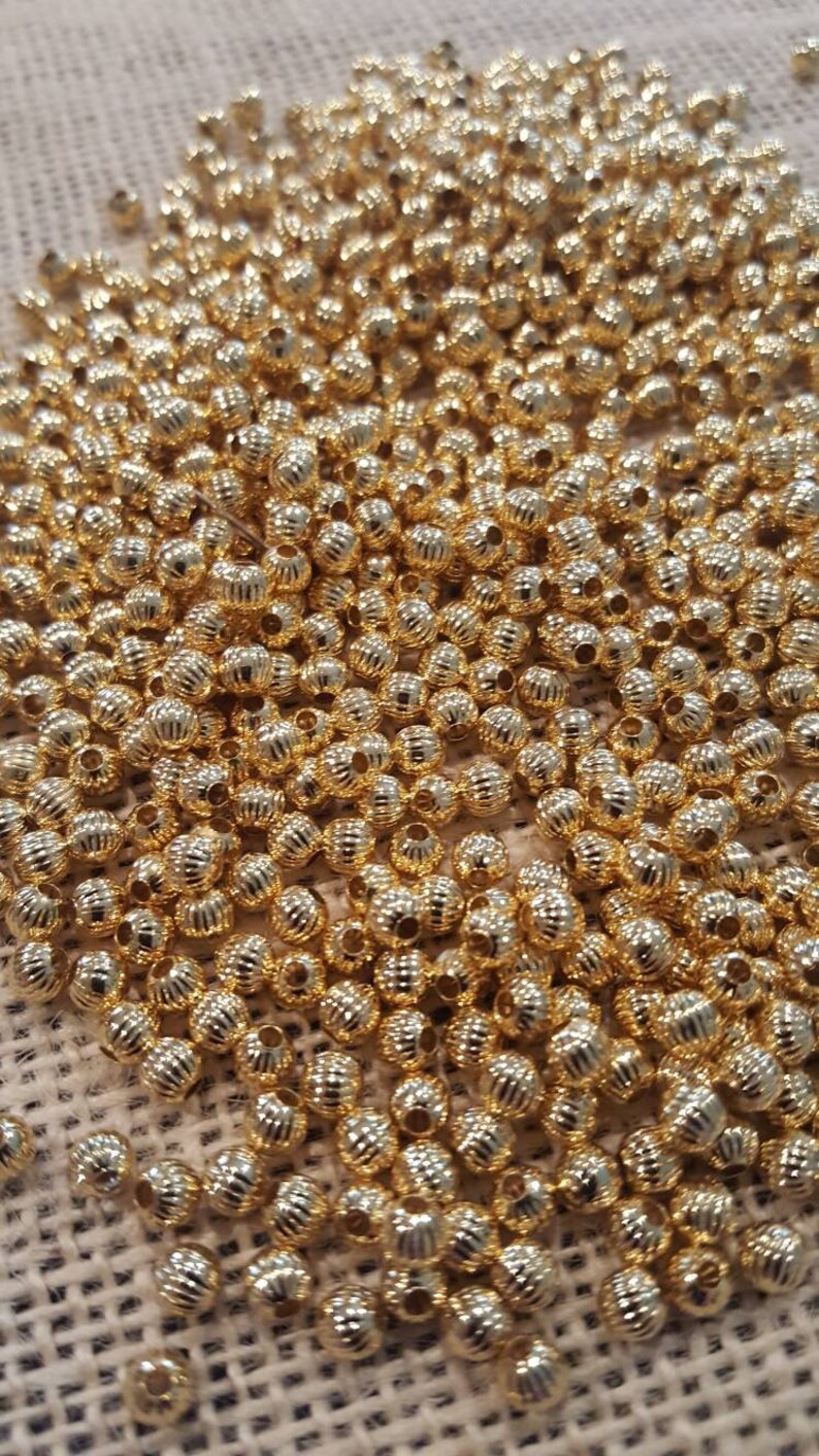 May include: A large pile of gold-colored metal beads. The beads are round and have a textured surface.