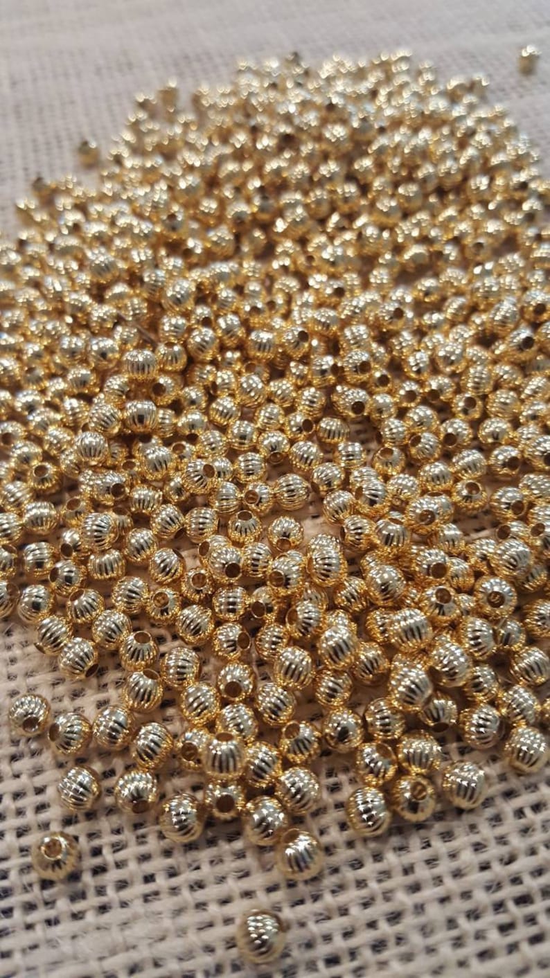 May include: A large pile of gold-colored metal beads. The beads are round and have a textured surface.