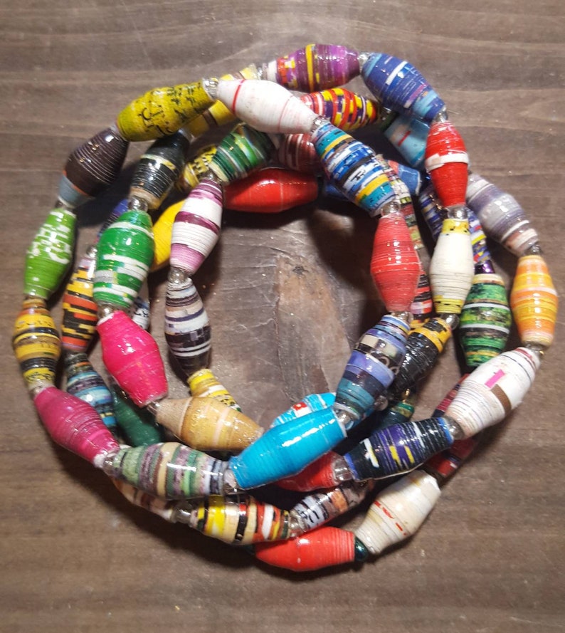 Op de afbeelding: Een kleurrijke ketting gemaakt van gerolde papier kralen. De kralen zijn in verschillende kleuren, waaronder rood, blauw, groen, geel en paars. De ketting is geregen op een zilveren koord.