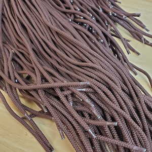 May include: A large bundle of brown shoelaces with silver aglets. The shoelaces are arranged in a random pattern and are all the same length.