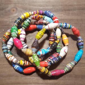 Op de afbeelding: Een kleurrijke ketting gemaakt van gerolde papier kralen. De kralen zijn in verschillende kleuren, waaronder rood, geel, blauw, groen en paars. De ketting is gelaagd en heeft een unieke, handgemaakte uitstraling.