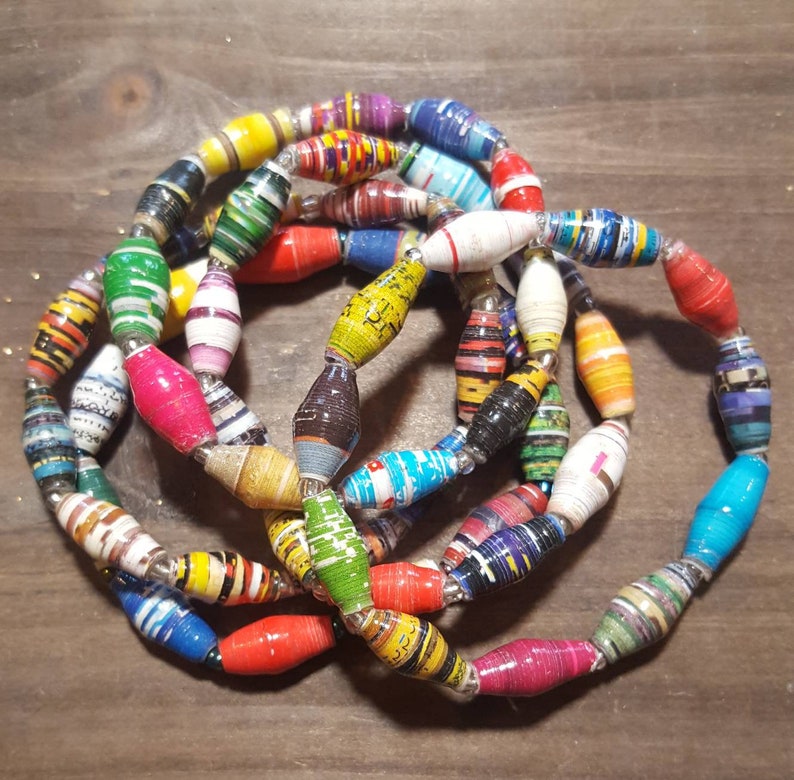 Op de afbeelding: Een kleurrijke ketting gemaakt van gerolde papier kralen. De kralen zijn in verschillende kleuren, waaronder rood, geel, blauw, groen en paars. De ketting is gelaagd en heeft een unieke, handgemaakte uitstraling.